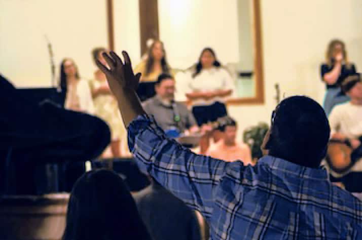 Worship at Agape Church A man in the congregation raises his hand in worship during a service at Agape Church, with the worship team leading on stage in the background.